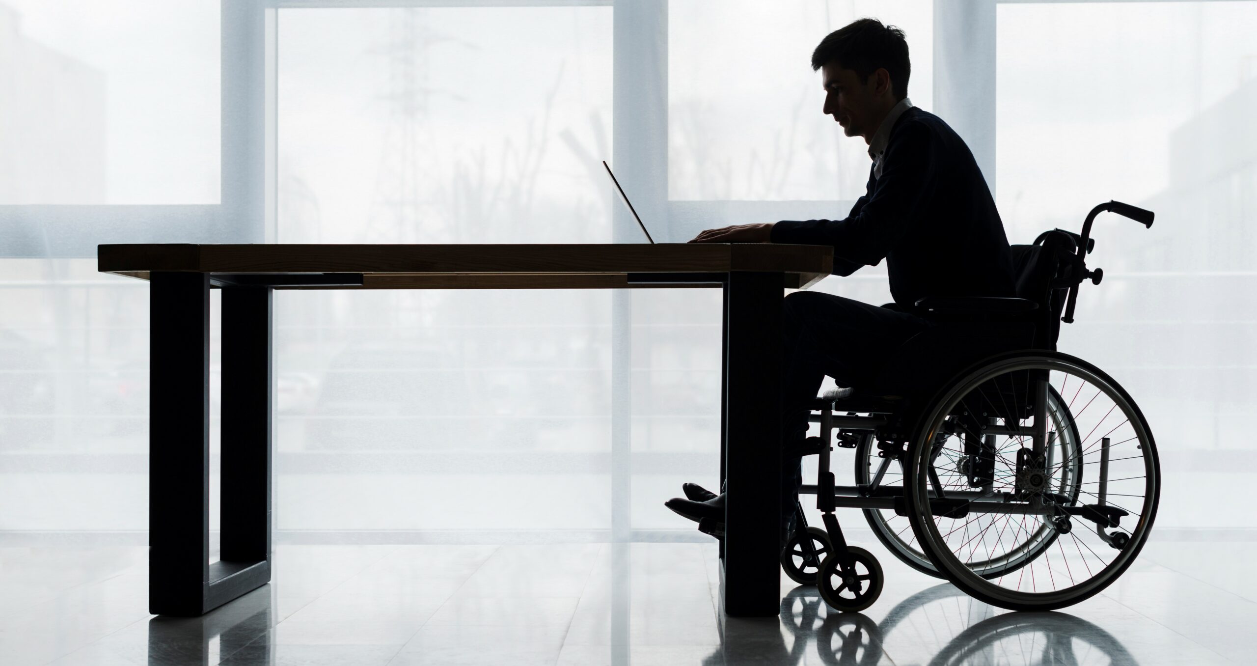 silhouette-businessman-sitting-wheelchair-using-laptop-table-front-window - Copy