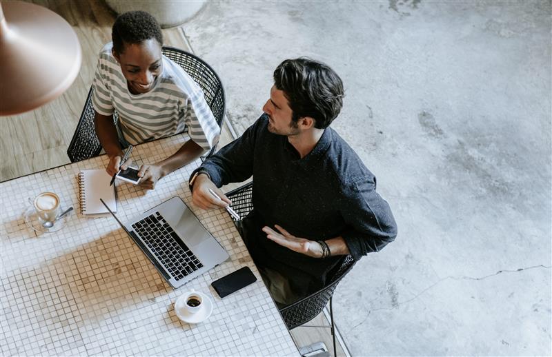 duas pessoas a conversar sentadas numa mesa de trabalho